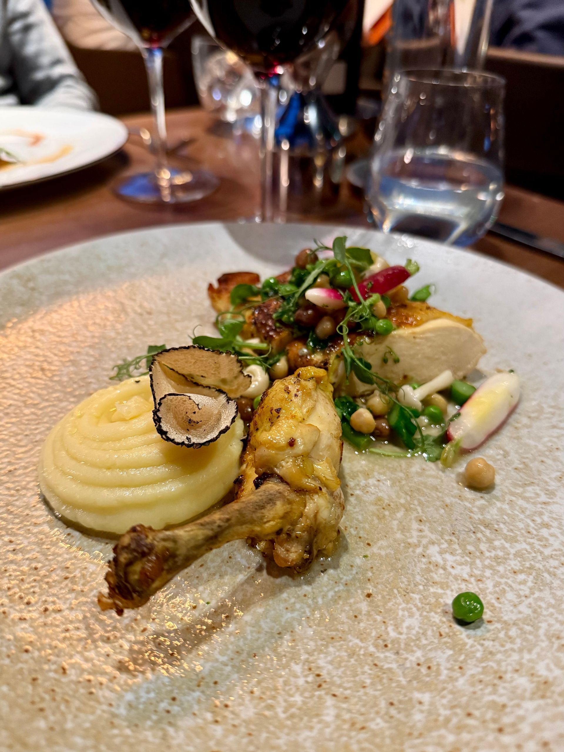 Gourmet plated dish at Fenchurch in London with mashed potatoes, roasted chicken, peas, and herbs on a restaurant table