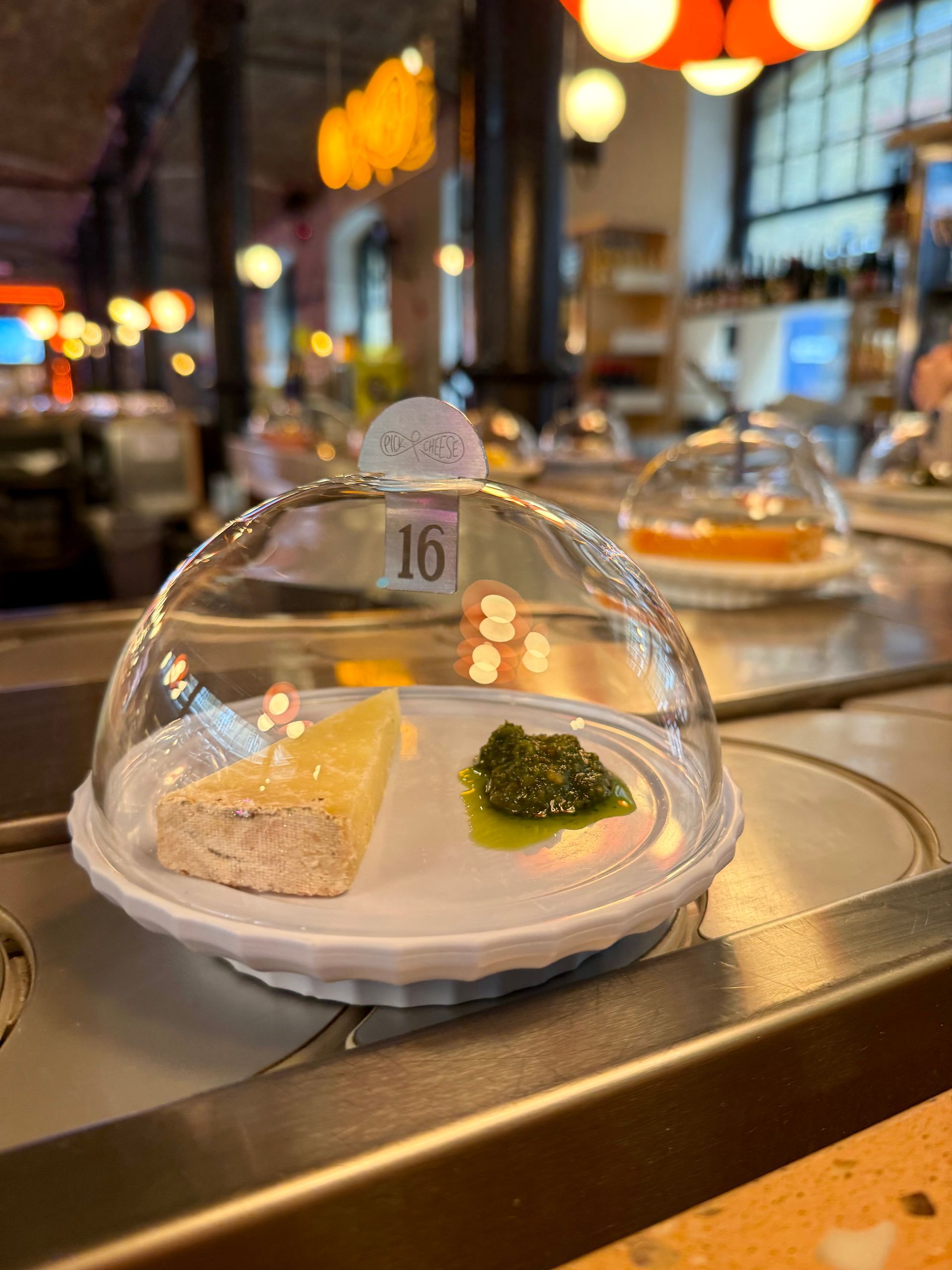 Cheese under glass dome on a restaurant table at Pick and Cheese in London at Seven Dials Market, with warm lights and a blurred dining room background
