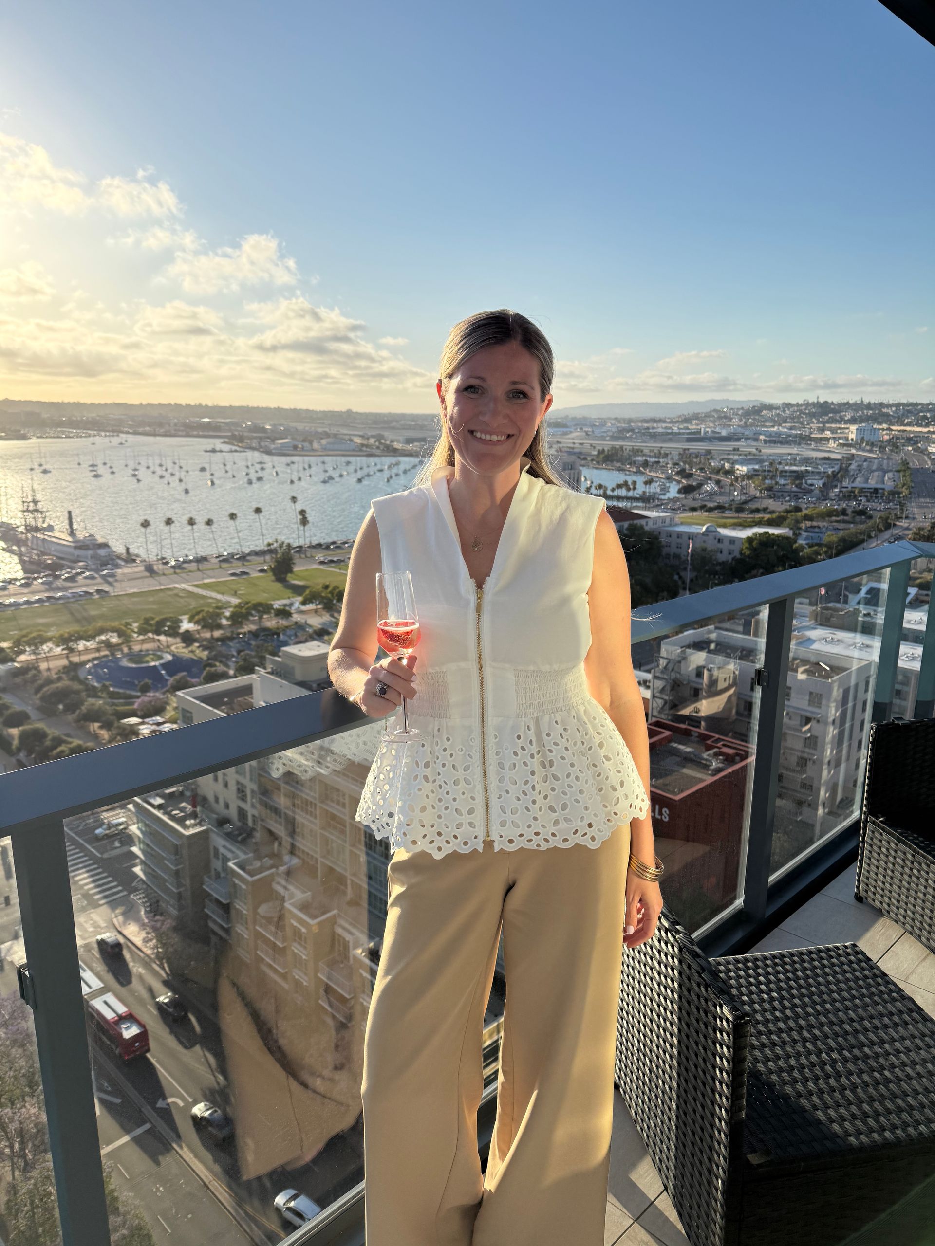 Woman standing on a balcony at sunset in San Diego, CA, holding a drink with a harbor view behind her.
