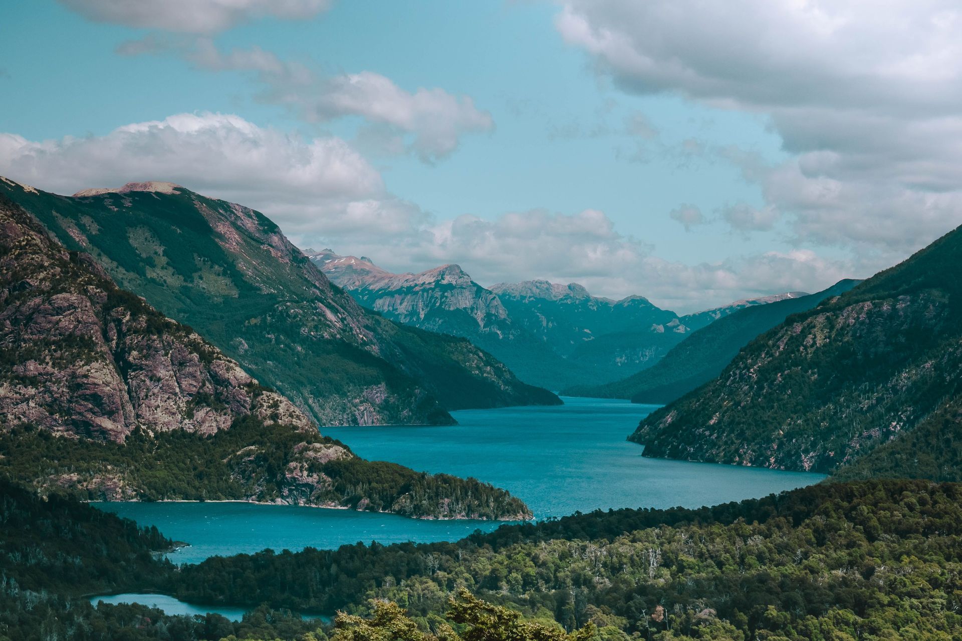 Turquoise mountain lake between rocky green hills under a cloudy sky in Patagonia