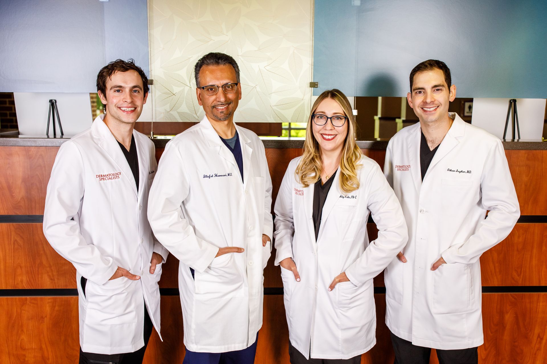Four medical professionals in white coats, posing indoors with smiles.