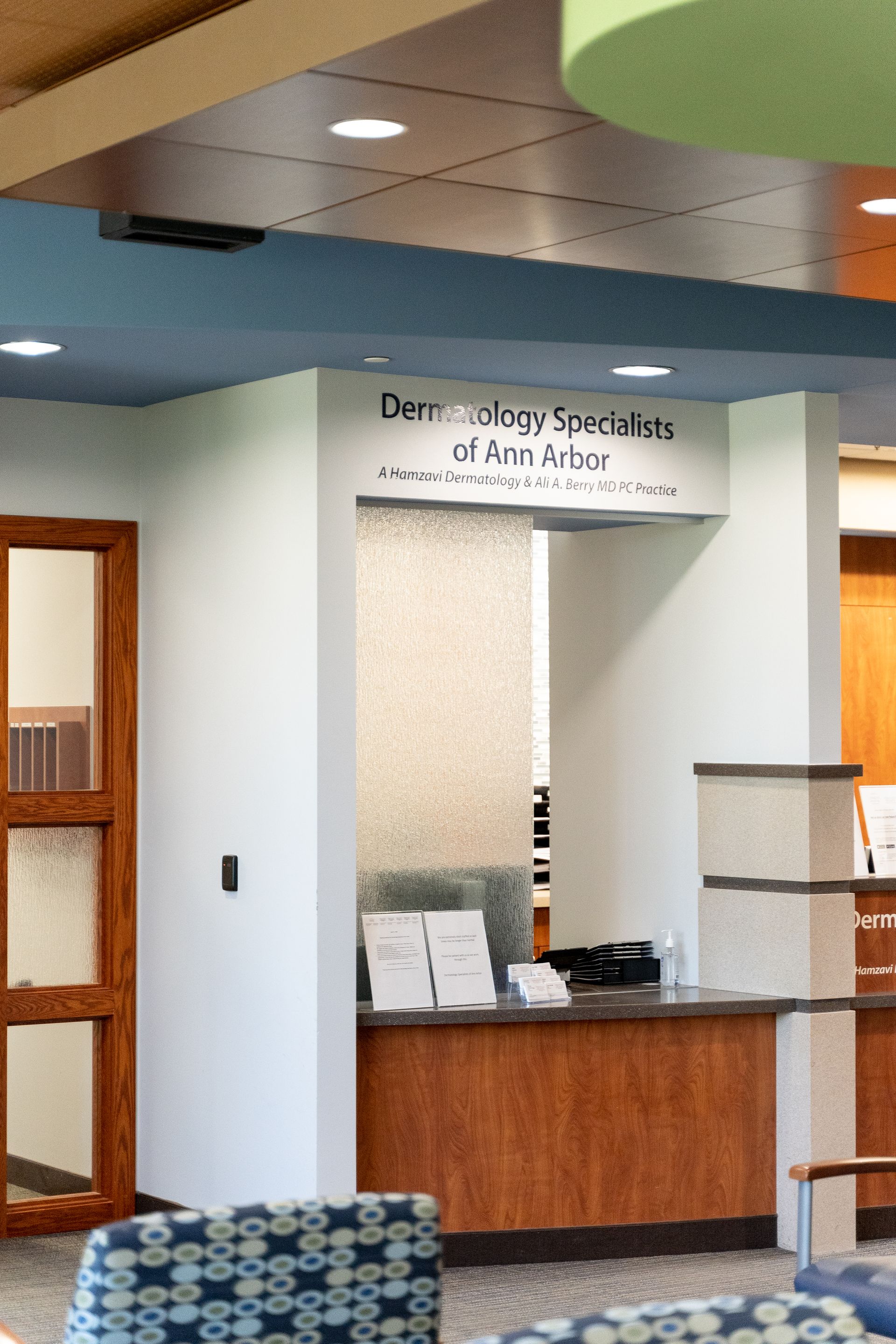 Reception desk for Dermatology Specialties of Ann Arbor with wooden counter, glass panel, and sign.