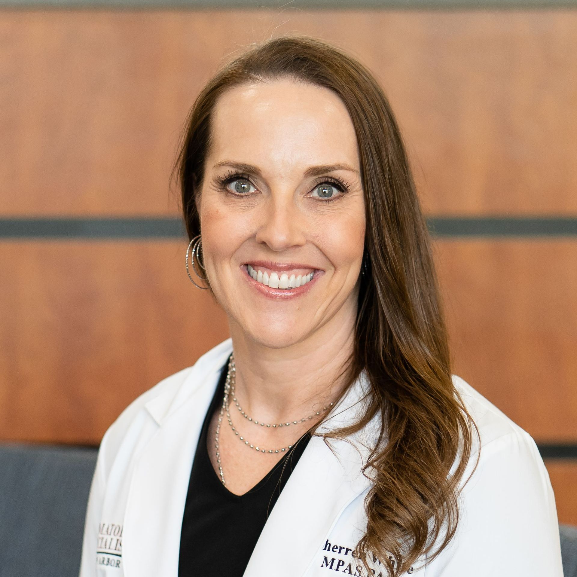 Smiling woman in a white coat, standing indoors.