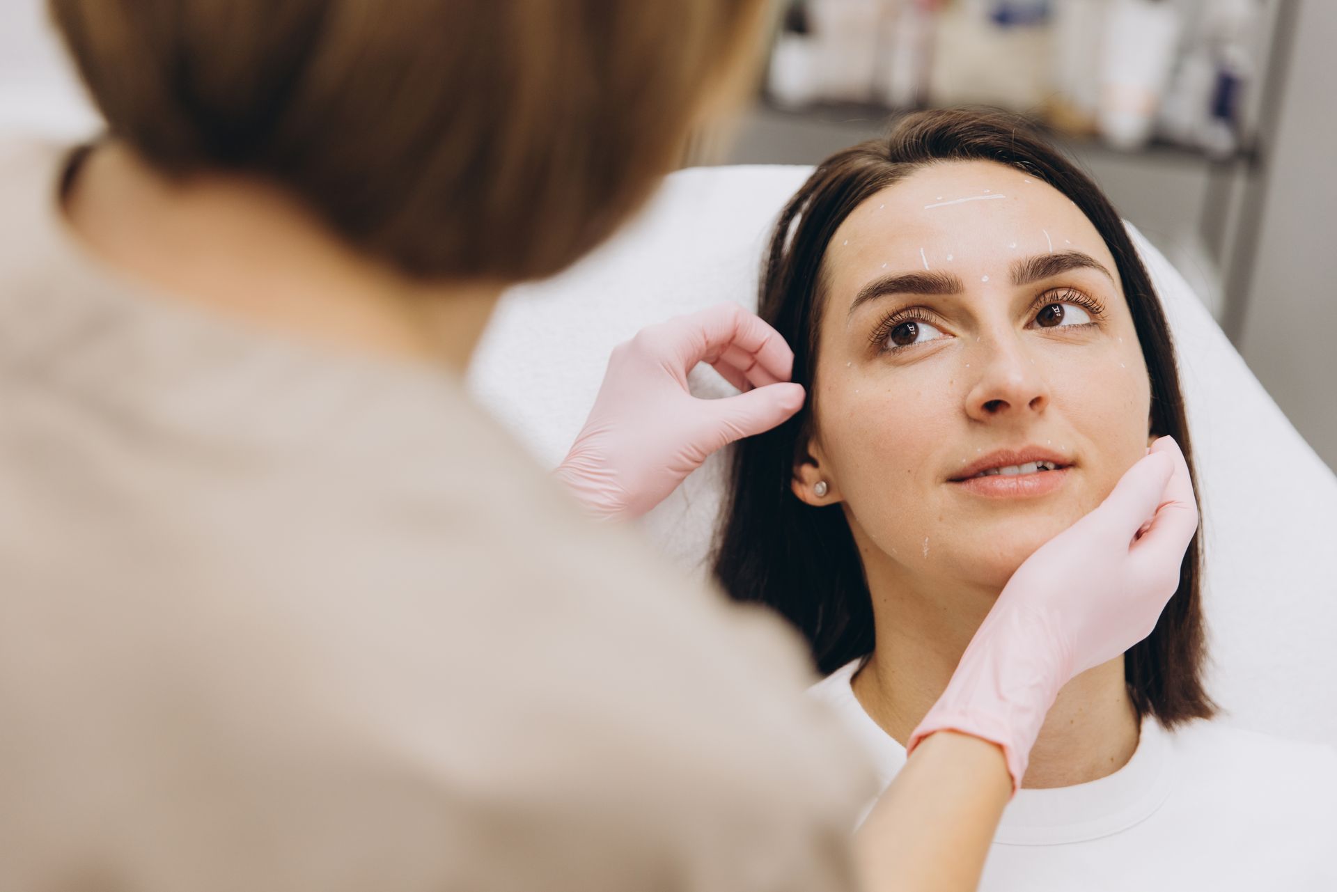 Cosmetologist marking woman's face before cosmetic injections in clinic