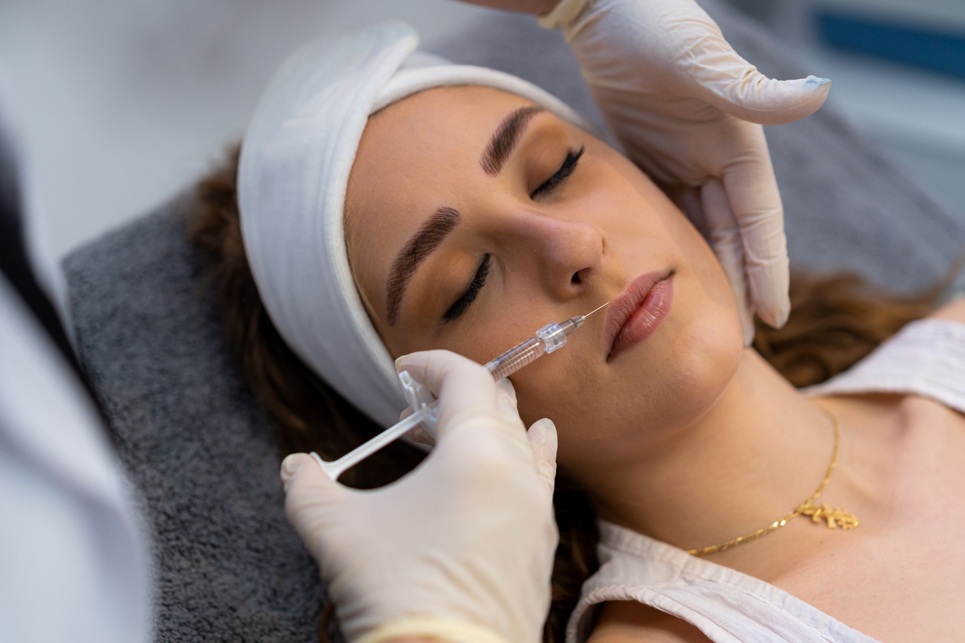 Woman with closed eyes receiving a lip filler injection from a gloved provider