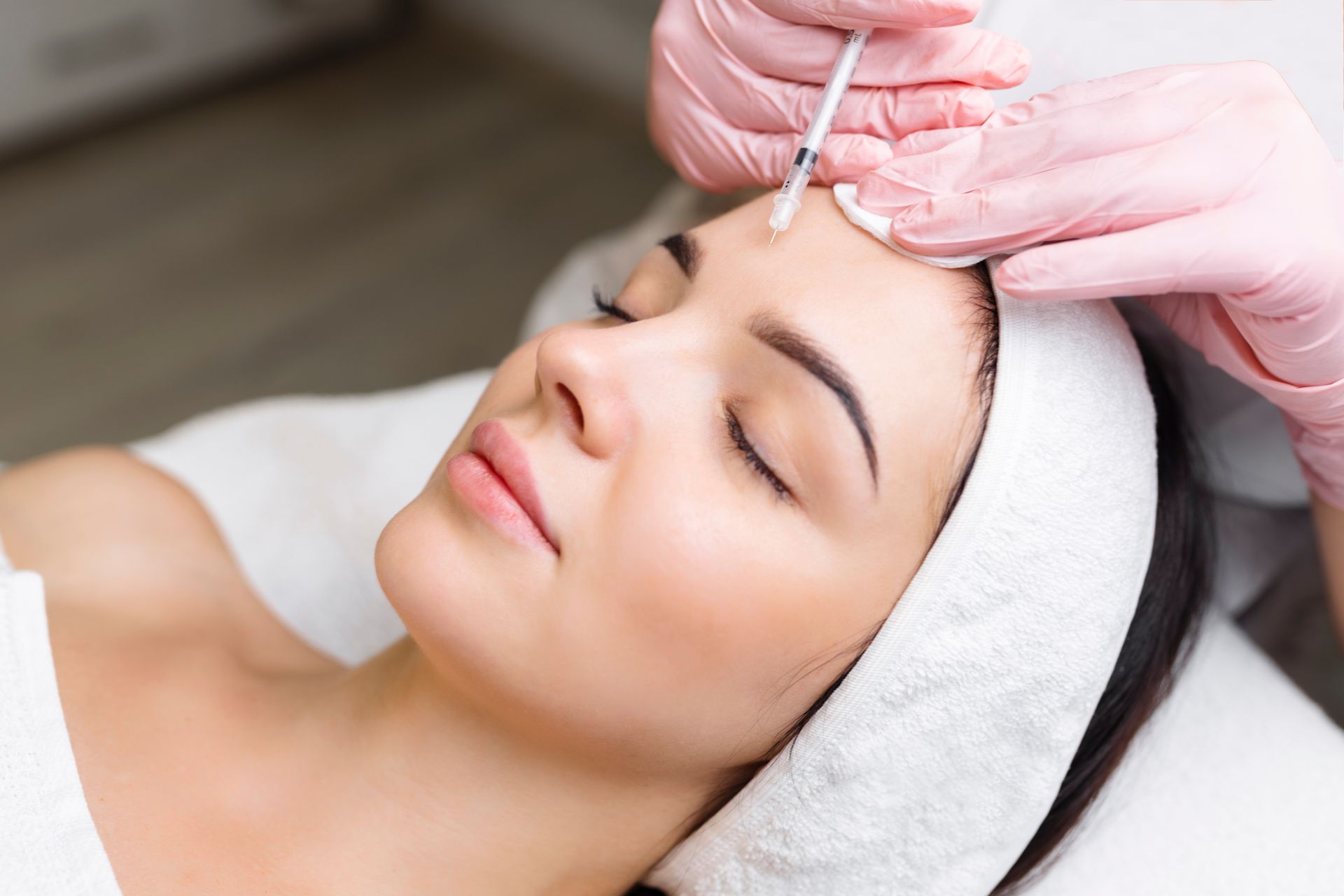Close up of hands of young cosmetologist injecting botox in female face.