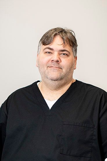 Man in black scrubs smiles, neutral background.