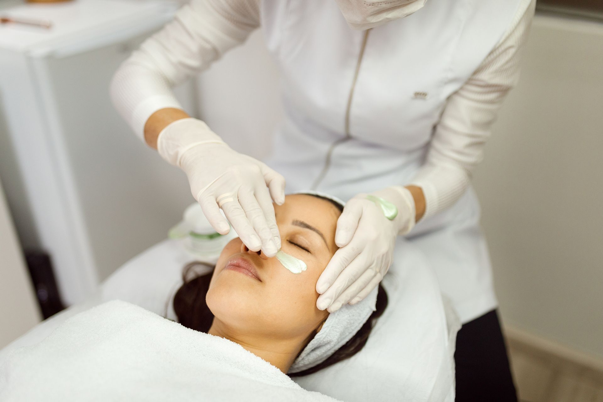 A woman gets an acne dermatology treatment at a beauty salon as a beautician works on her skin.