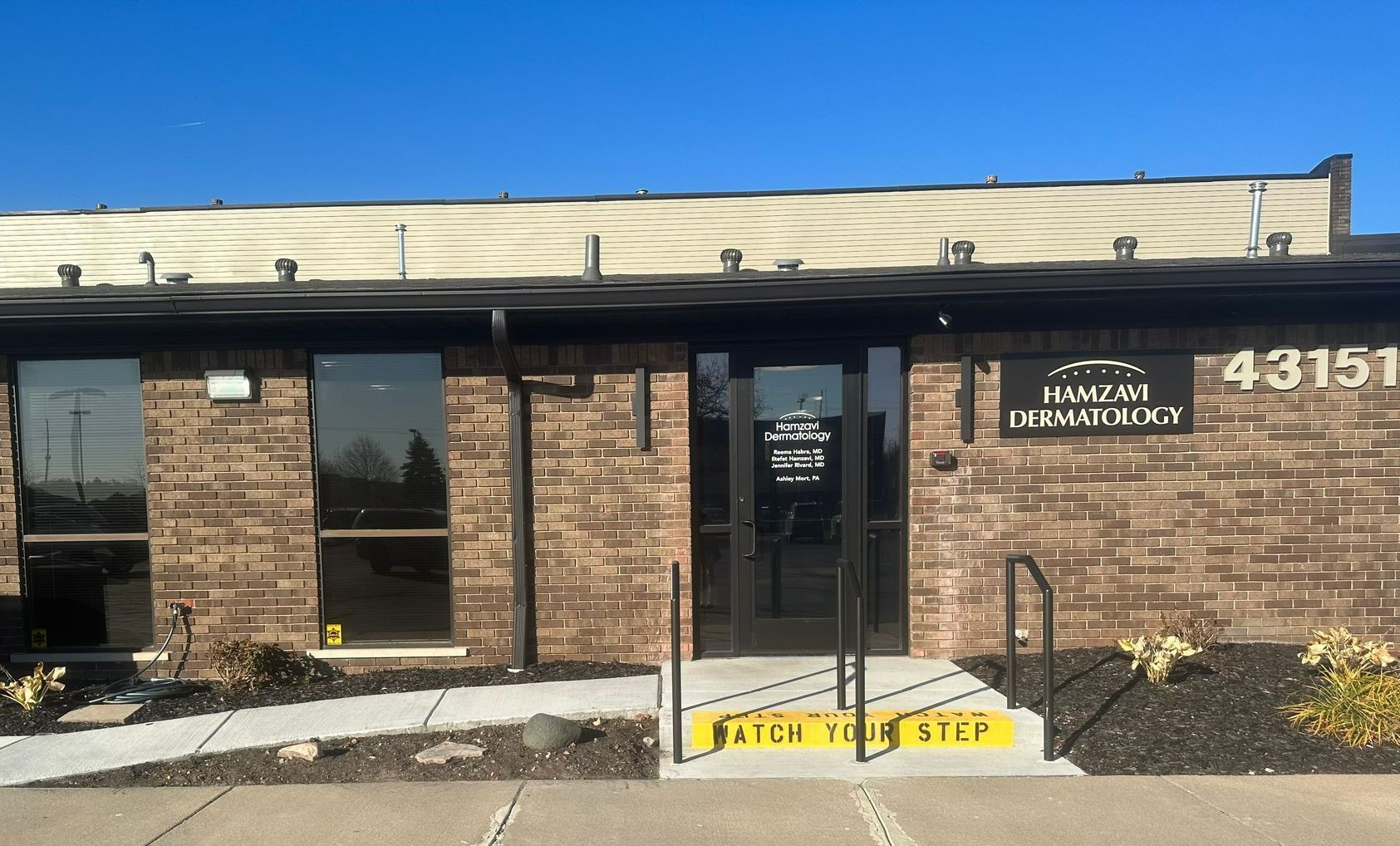 Exterior view of an office building with brick facade, glass windows and doors. Text over door,