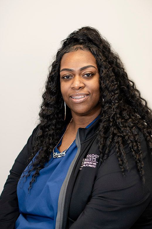 Woman with curly hair, wearing a blue shirt and black jacket, smiling.