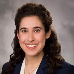 Smiling woman with dark curly hair wearing a blazer and white shirt.