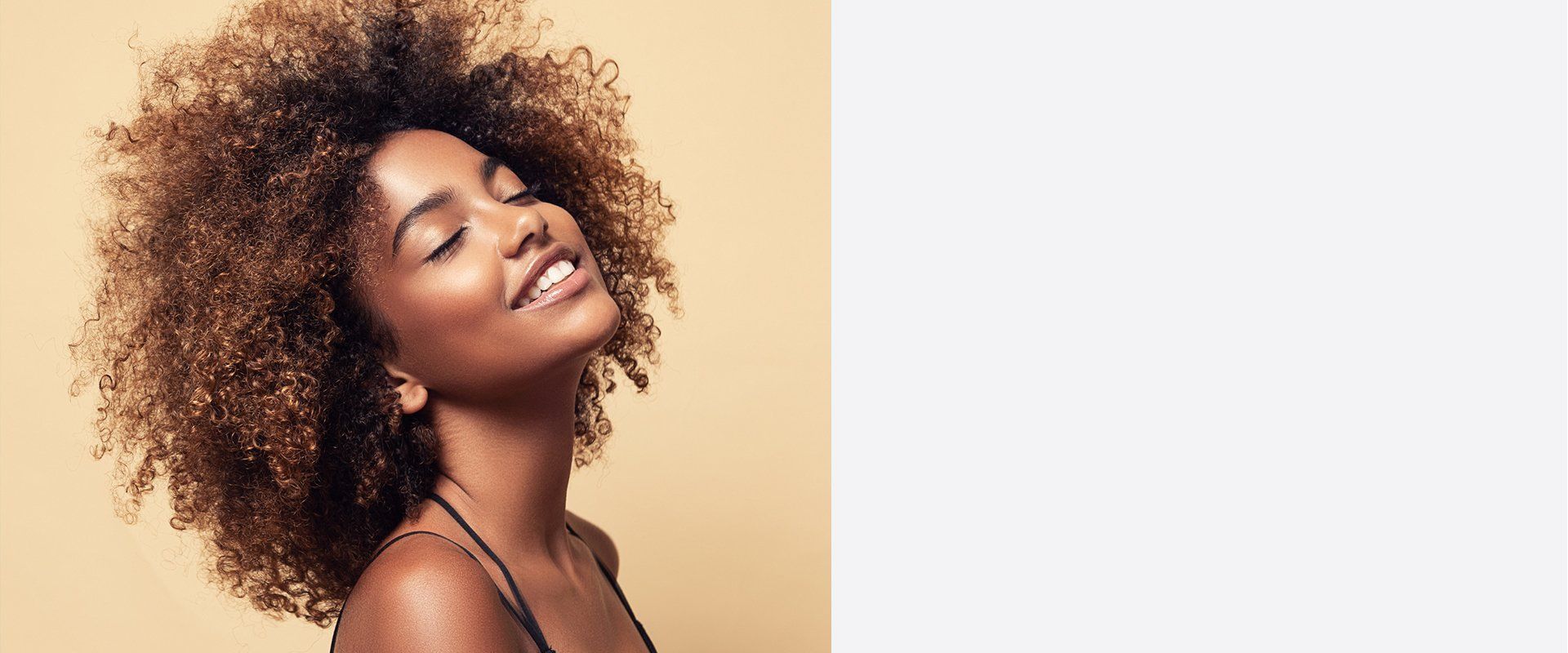 Woman with a bright smile and natural afro hair against a beige background.