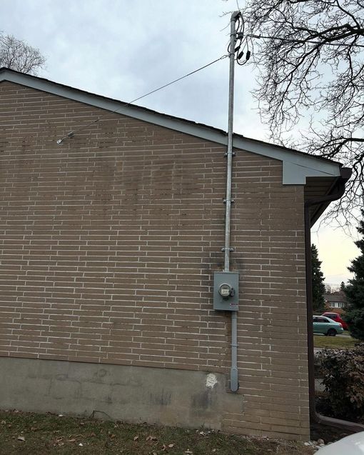Brick house side wall with a utility meter and vertical conduit under a blue sky