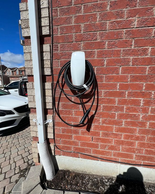 Coiled black cable mounted on a red brick wall beside a white drainpipe and parked car.