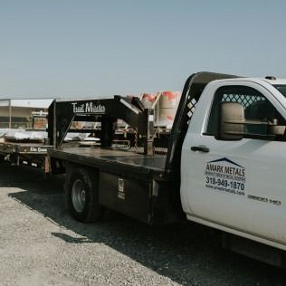 Flatbed tow truck with metal equipment parked on a gravel lot under a cloudy sky