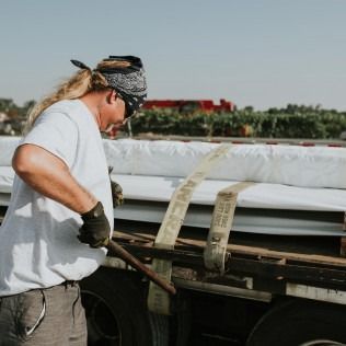 Worker in gloves tightening straps on a flatbed truck loaded with stacked materials outdoors