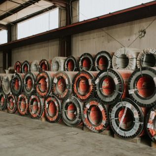 Stacks of large industrial cable reels with red centers stored in a warehouse.