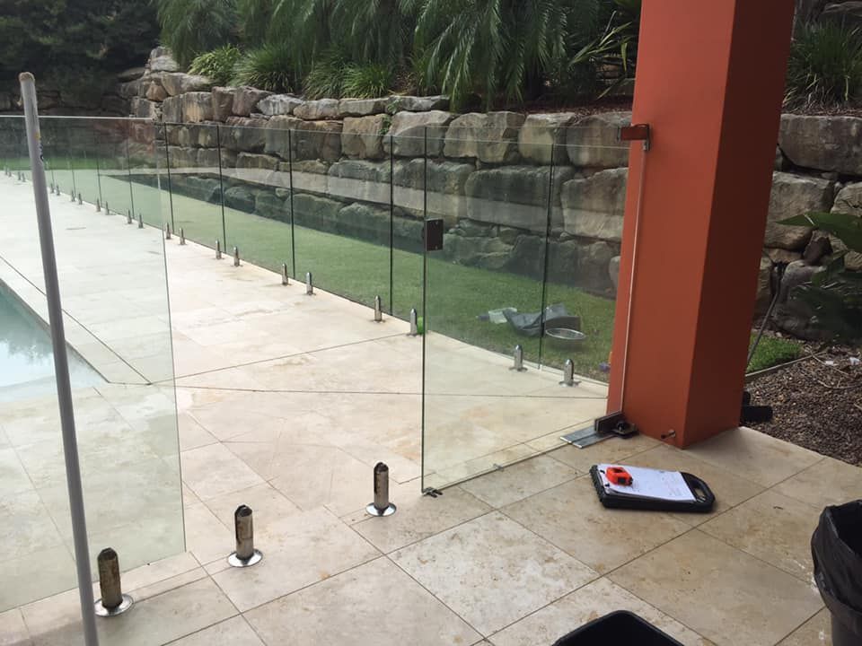 A Glass Fence Surrounds A Swimming Pool With A Brick Wall In The Background — Avoca Beach Glass In West Gosford, NSW