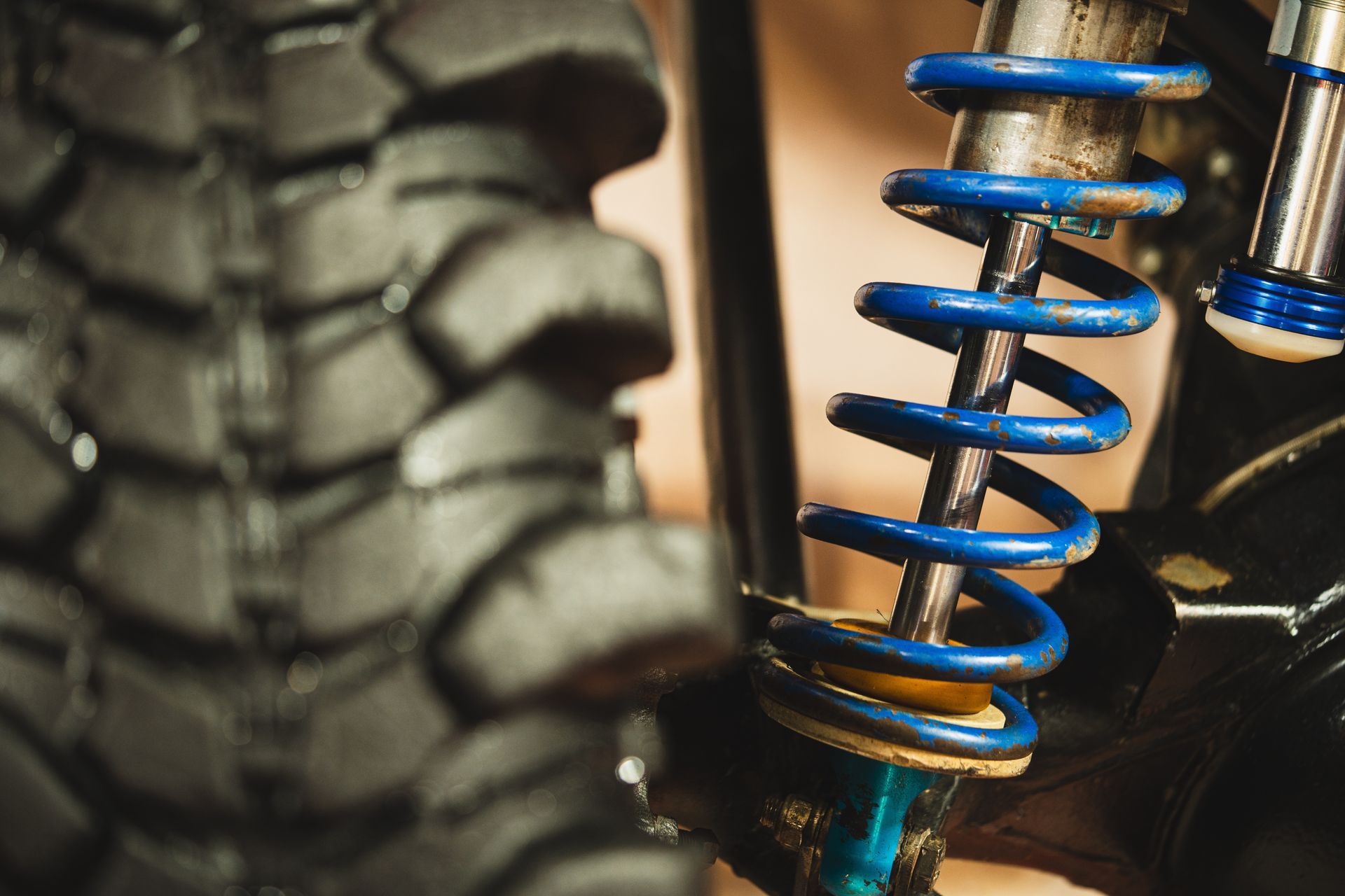Close-up of a dirt bike tire and blue suspension spring with mud-covered treads