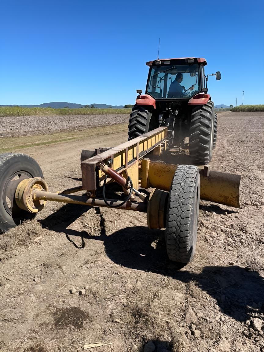 A Tractor Is Driving Down A Dirt Road With A Trailer Attached To It — Mackay Hose Fitting Services In West Mackay, QLD