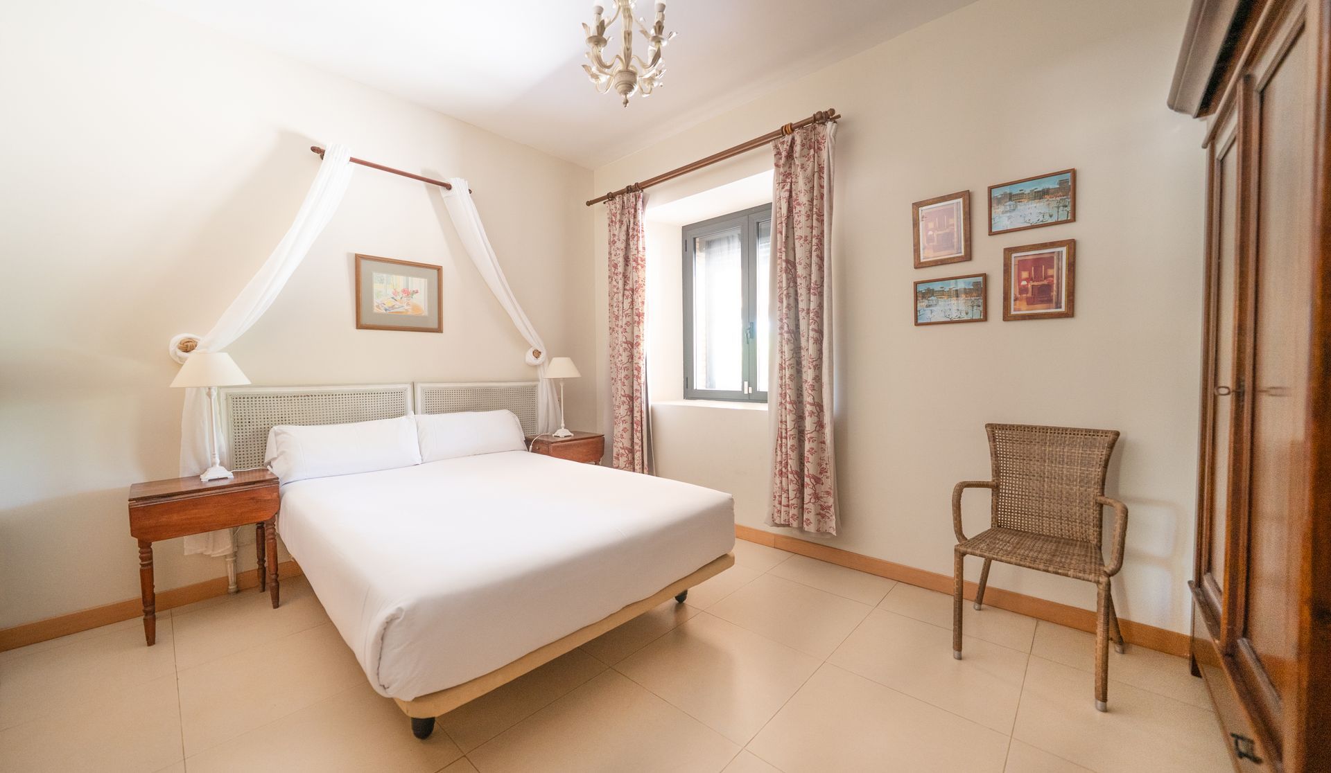 Habitación luminosa con cama, armario de madera, silla y cuadro enmarcado cerca de una ventana.