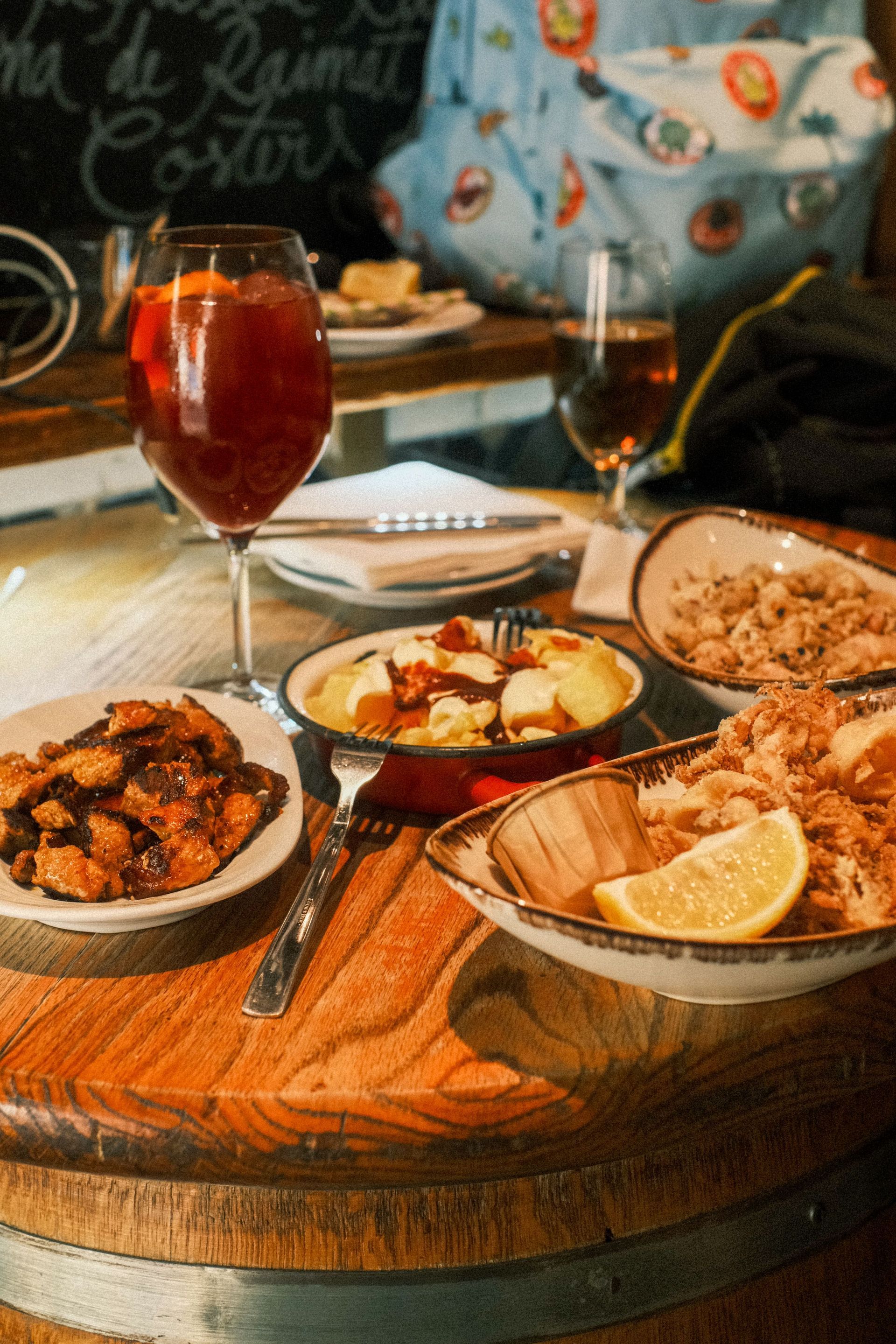 Mesa con varios platos y dos copas de vino tinto, en un ambiente cálido e informal.