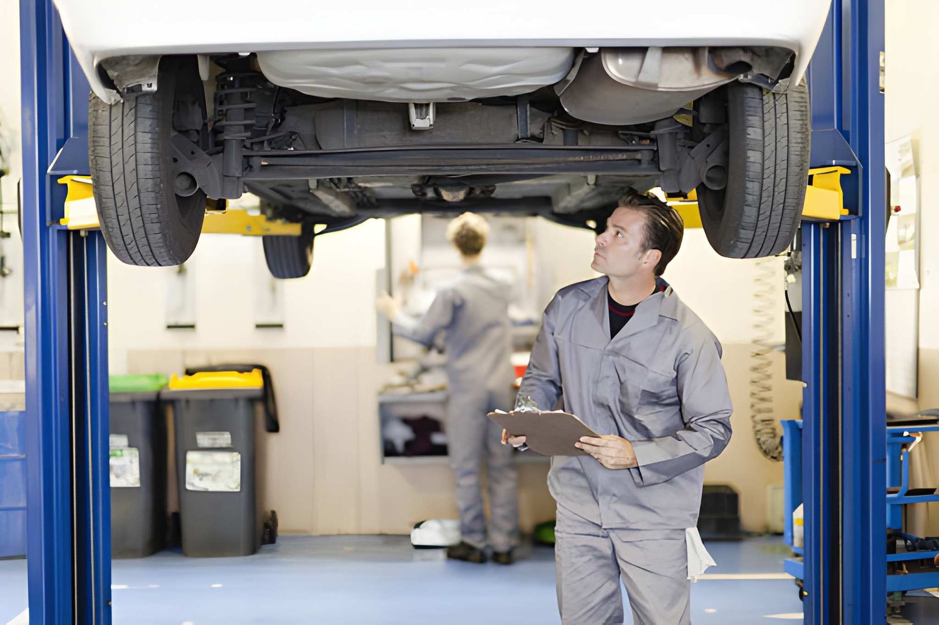 Mechanic inspecting car raised on a lift; another worker in the background, auto shop interior. | Premier Auto Service Center of SW Florida LLC
