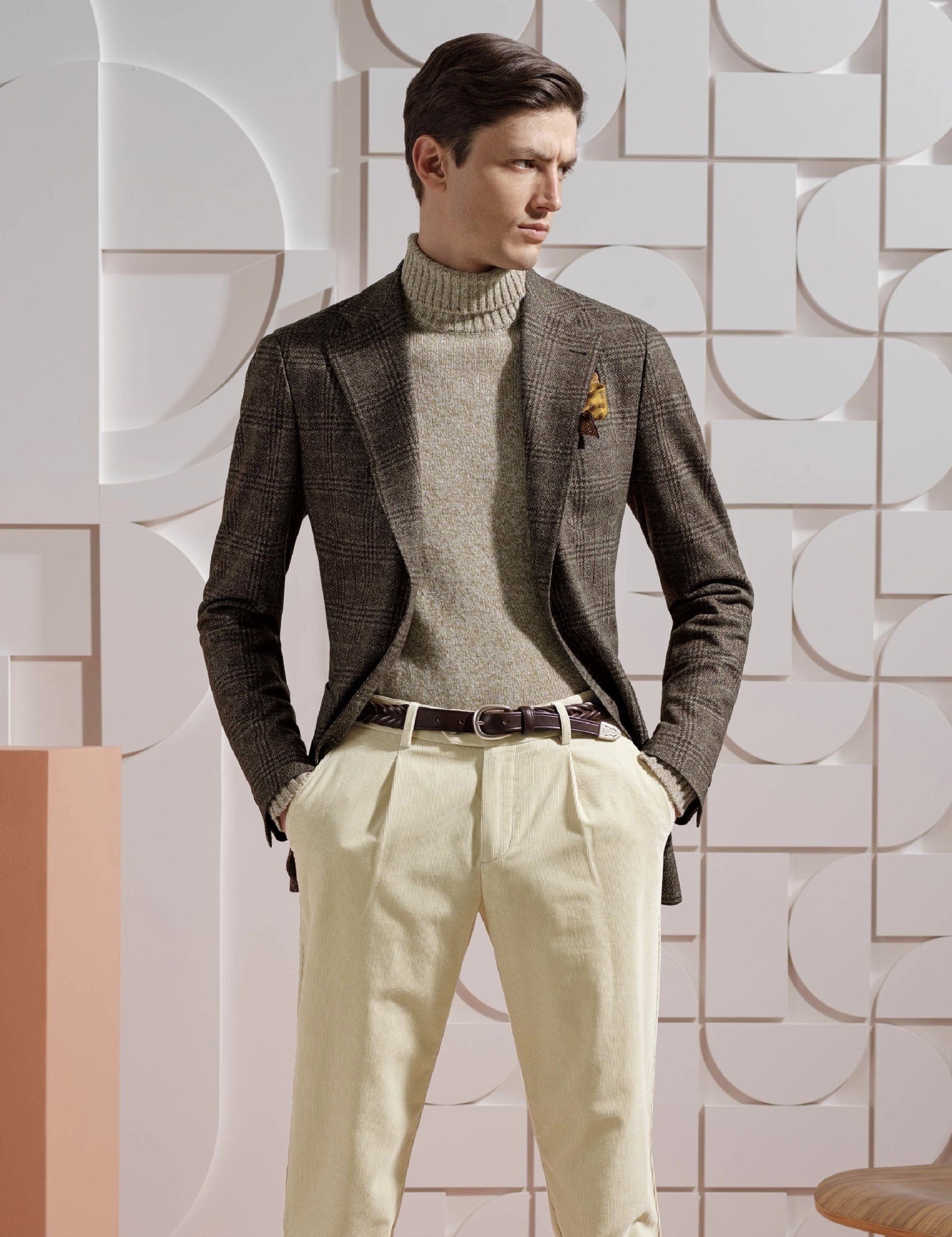 A man wearing a jacket and sweater is standing with his hands in his pockets.