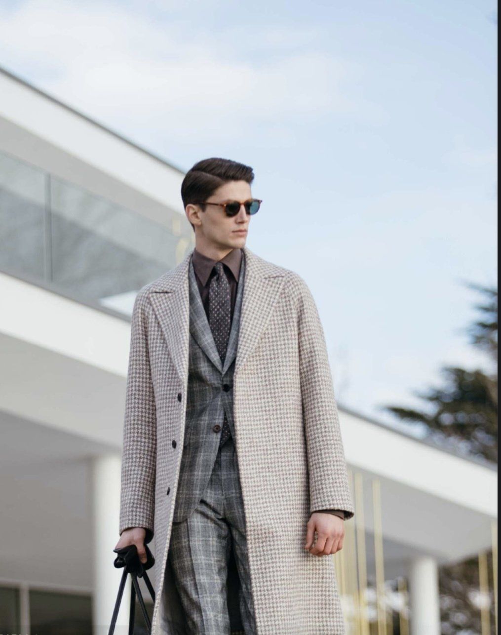 A man in a suit and coat is walking in front of a building.