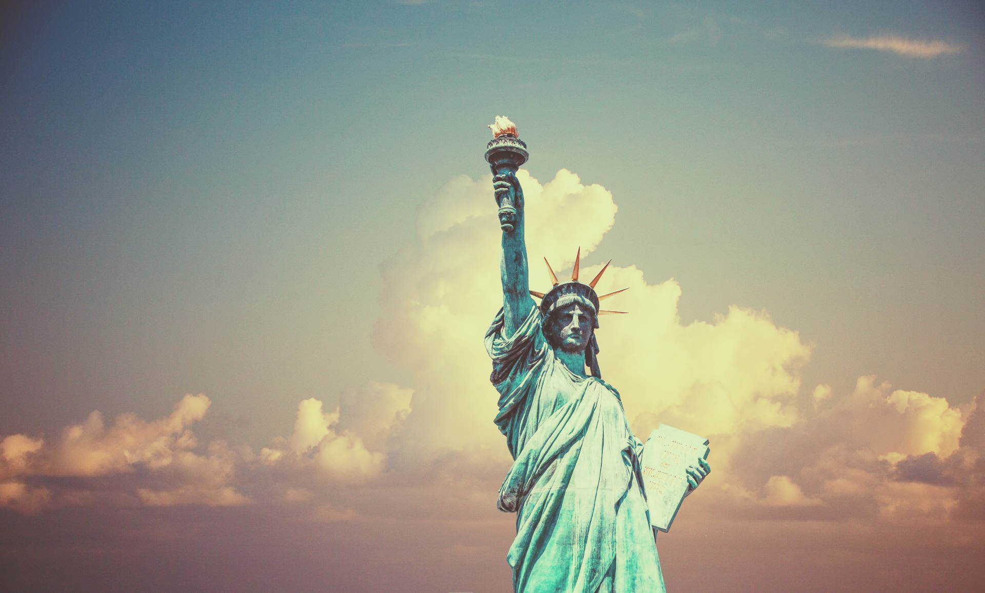 The statue of liberty is standing in front of a cloudy sky.