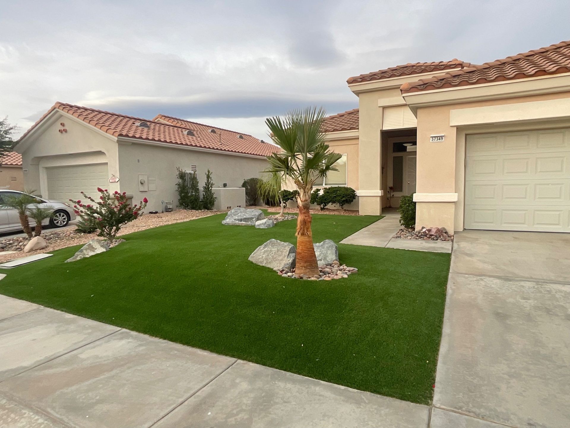 Desert-style suburban home with red-tile roofs, a green lawn, palm tree, and garage