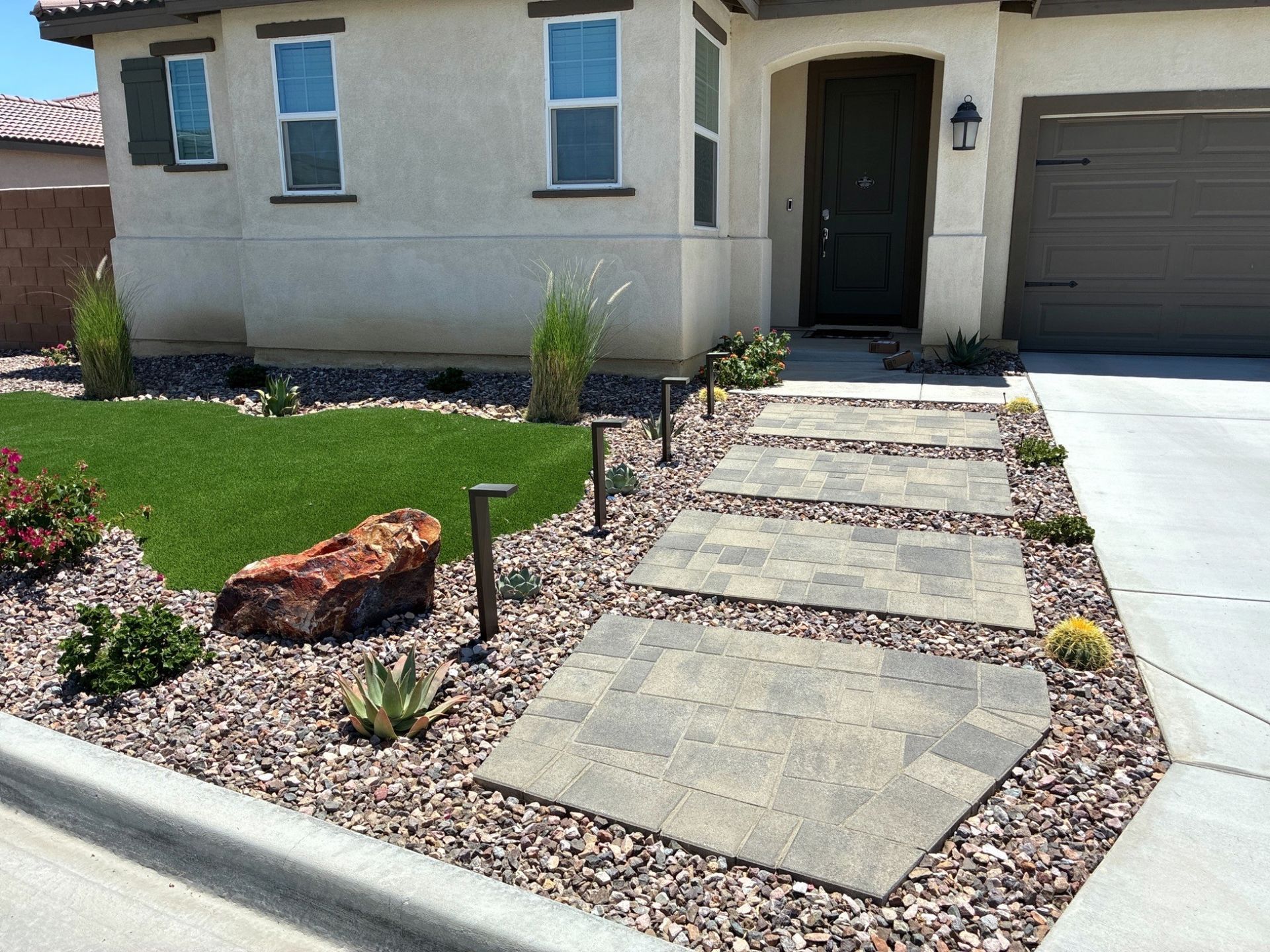Front walkway with stepping stones, desert landscaping, and a garage at a beige house entrance