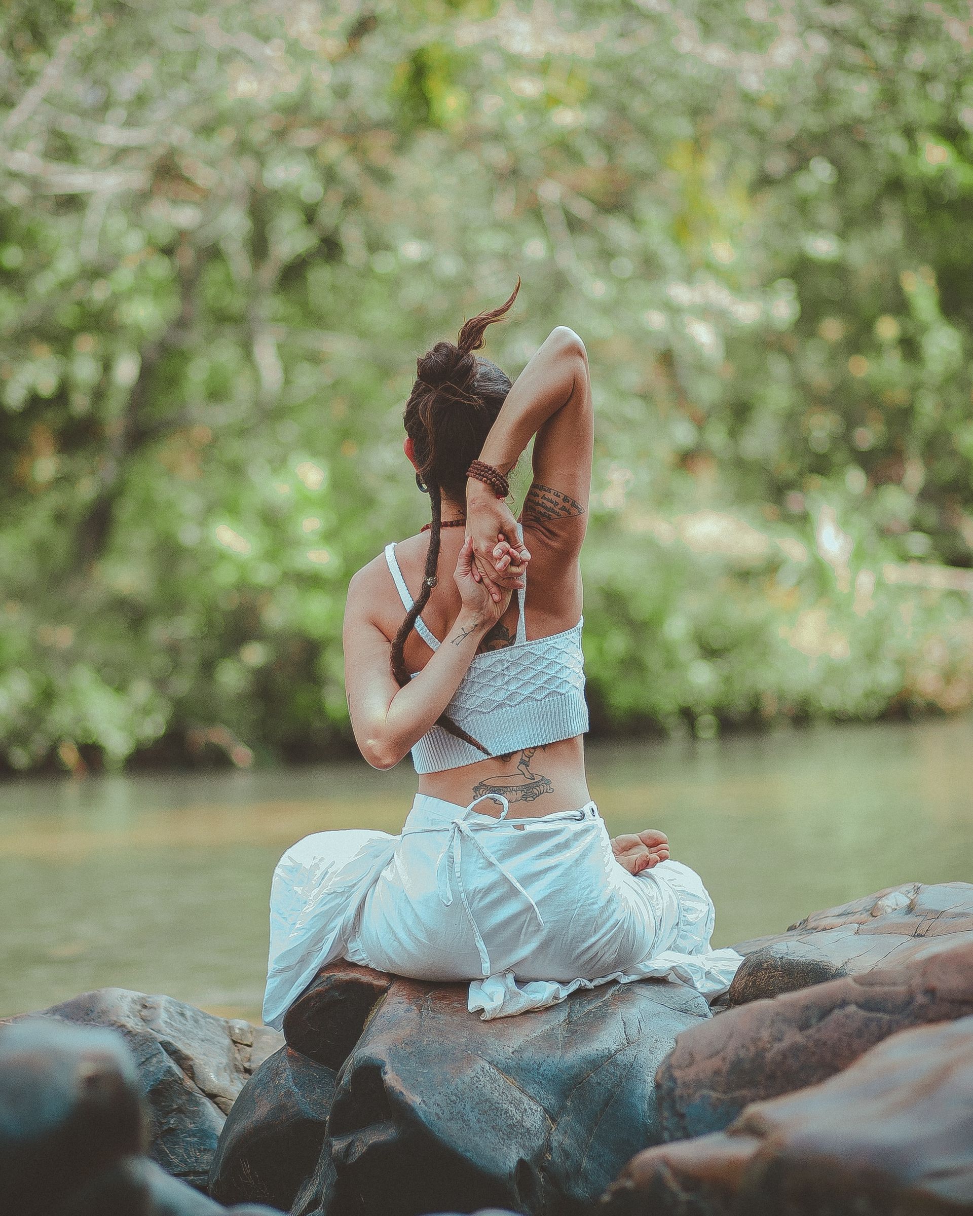 Una mujer está sentada sobre una roca cerca de un río estirando su espalda.