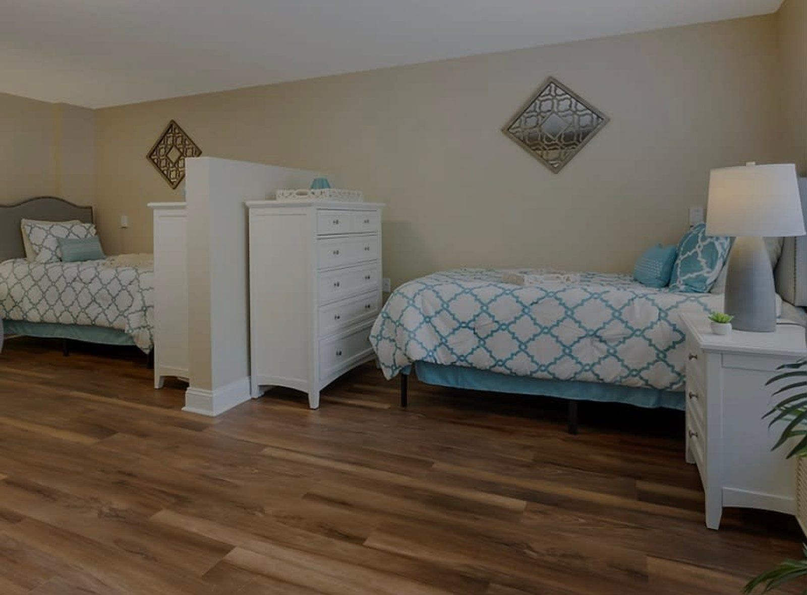 A shared bedroom in a senior living facility with two beds, white furniture, and teal accents.