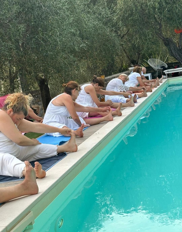 Persone vestite di bianco si stendono vicino a una piscina, sullo sfondo degli ulivi.