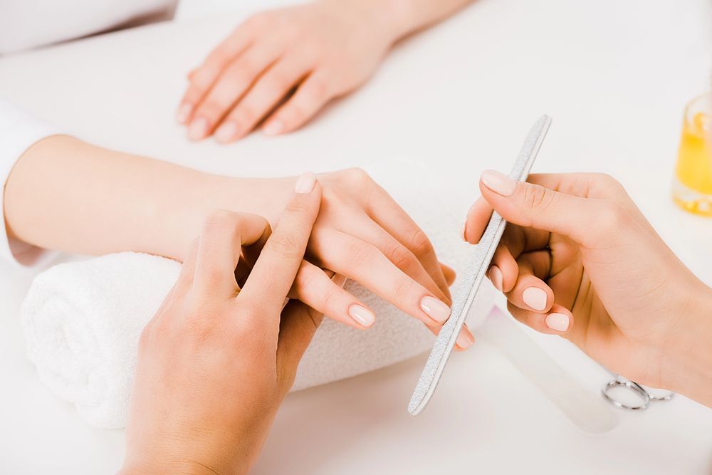 Persona che lima le unghie di un'altra persona al tavolo da manicure.