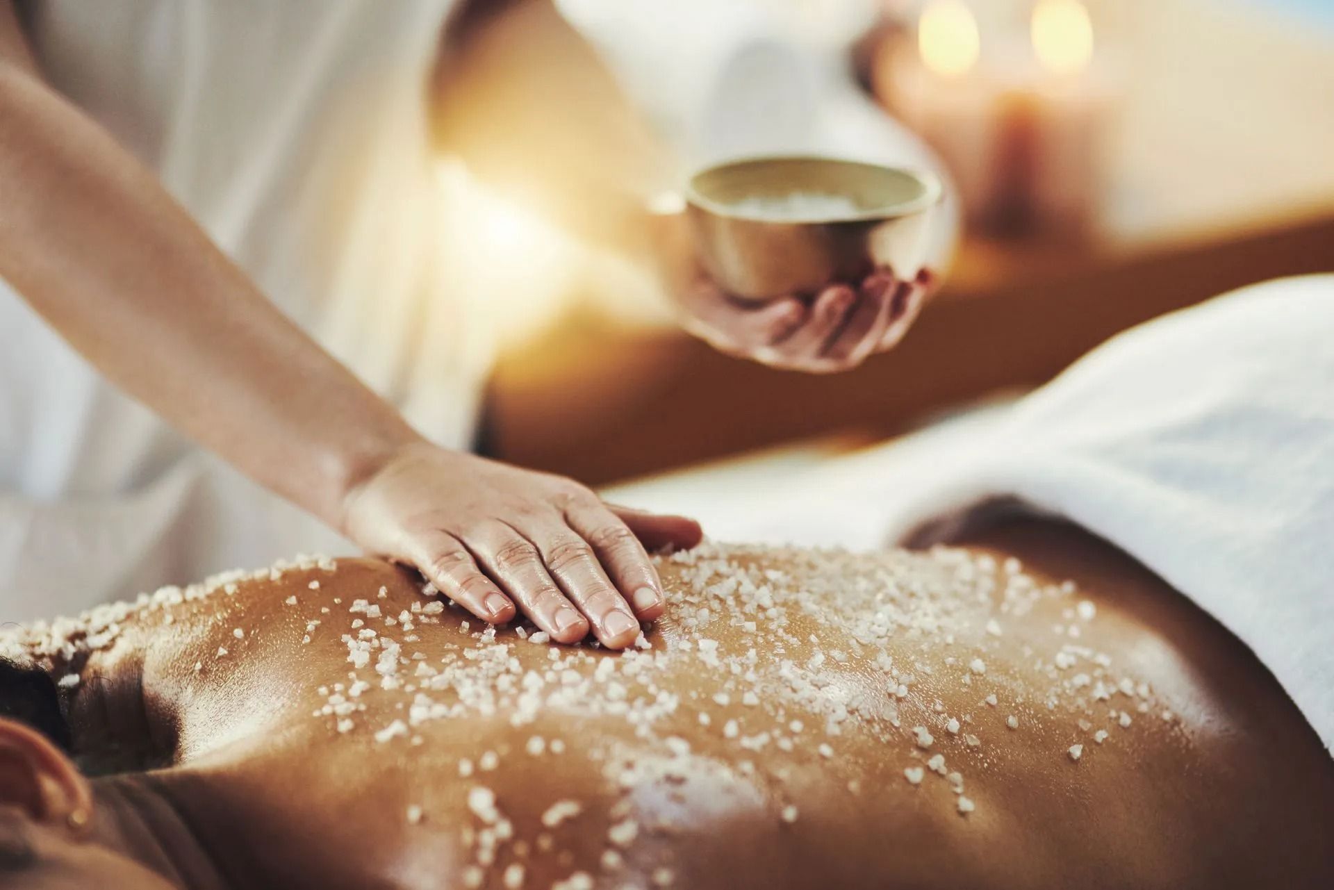 Persona che riceve un trattamento di scrub al sale in una spa, con candele sullo sfondo.