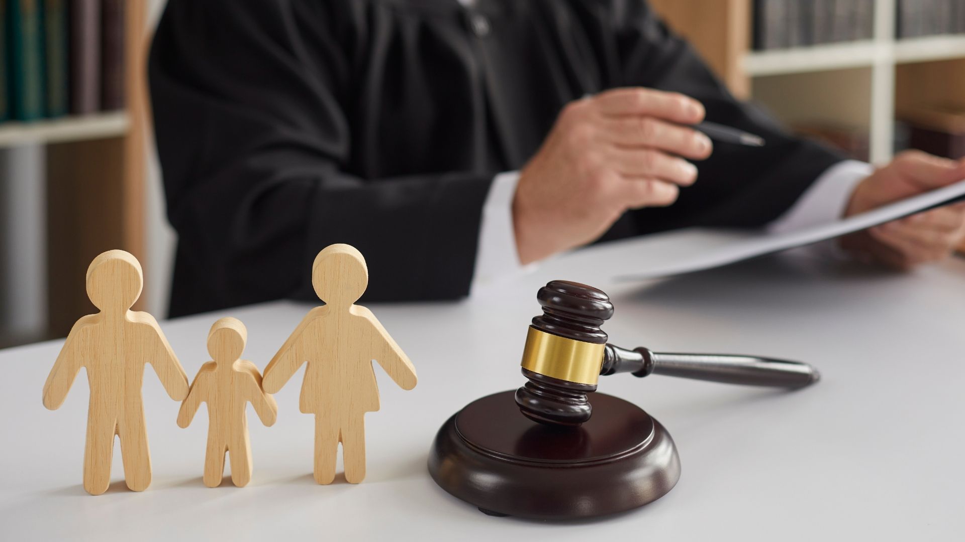 Family figurines beside a gavel on a desk, with a person reviewing documents in the background