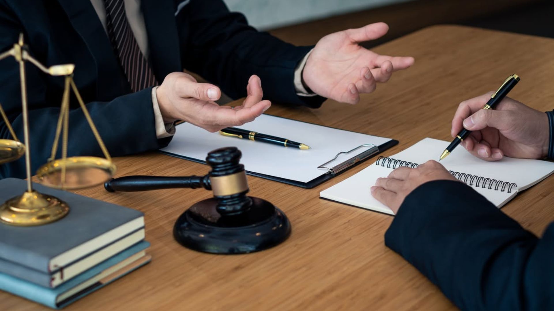 Lawyers discussing a case at a wooden desk with a gavel, scales of justice, and documents