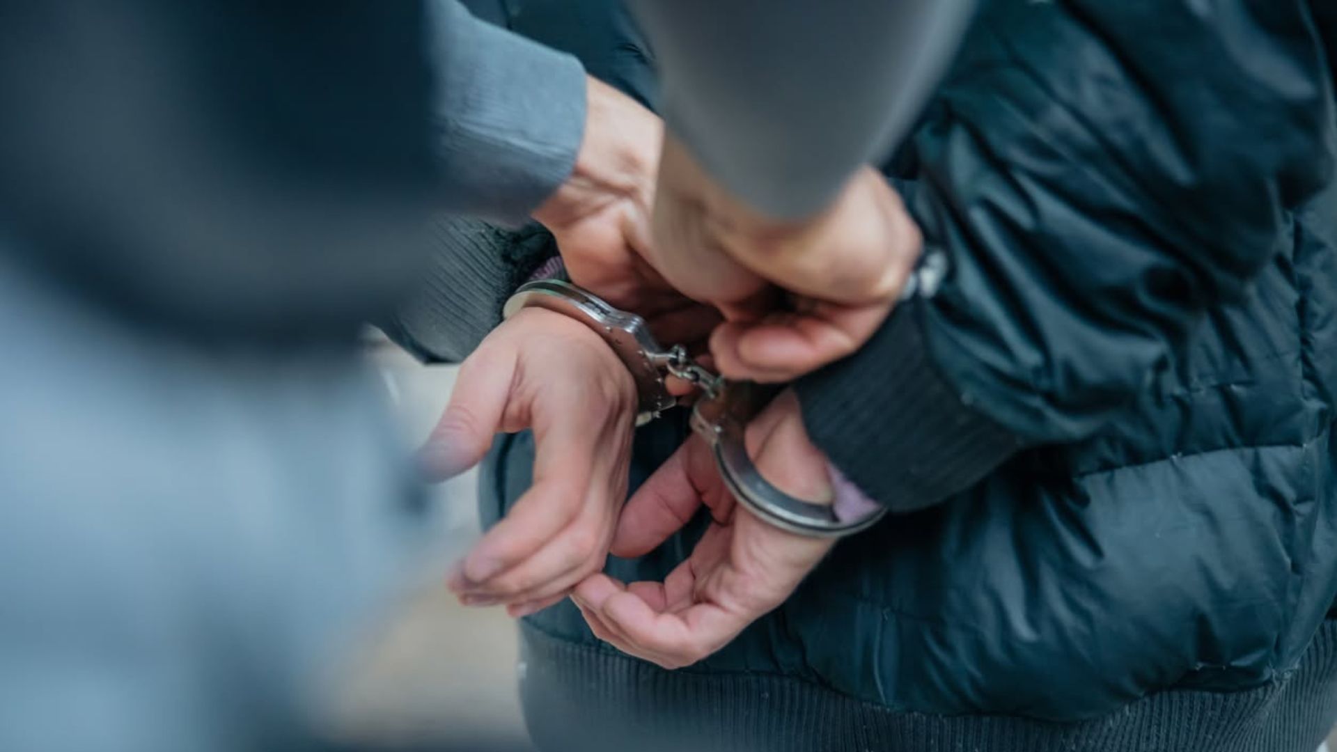 Hands in handcuffs being secured by another person in a dark jacket