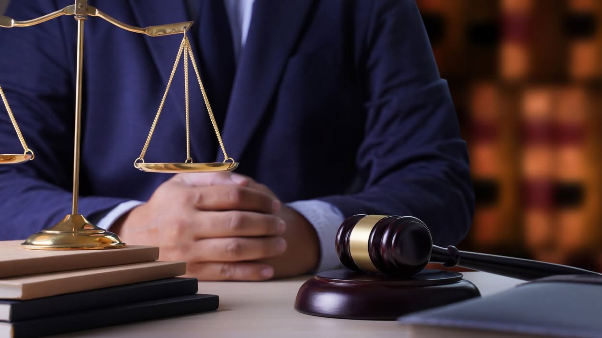 Judge’s gavel, balance scales, and hands on a desk in a courtroom setting