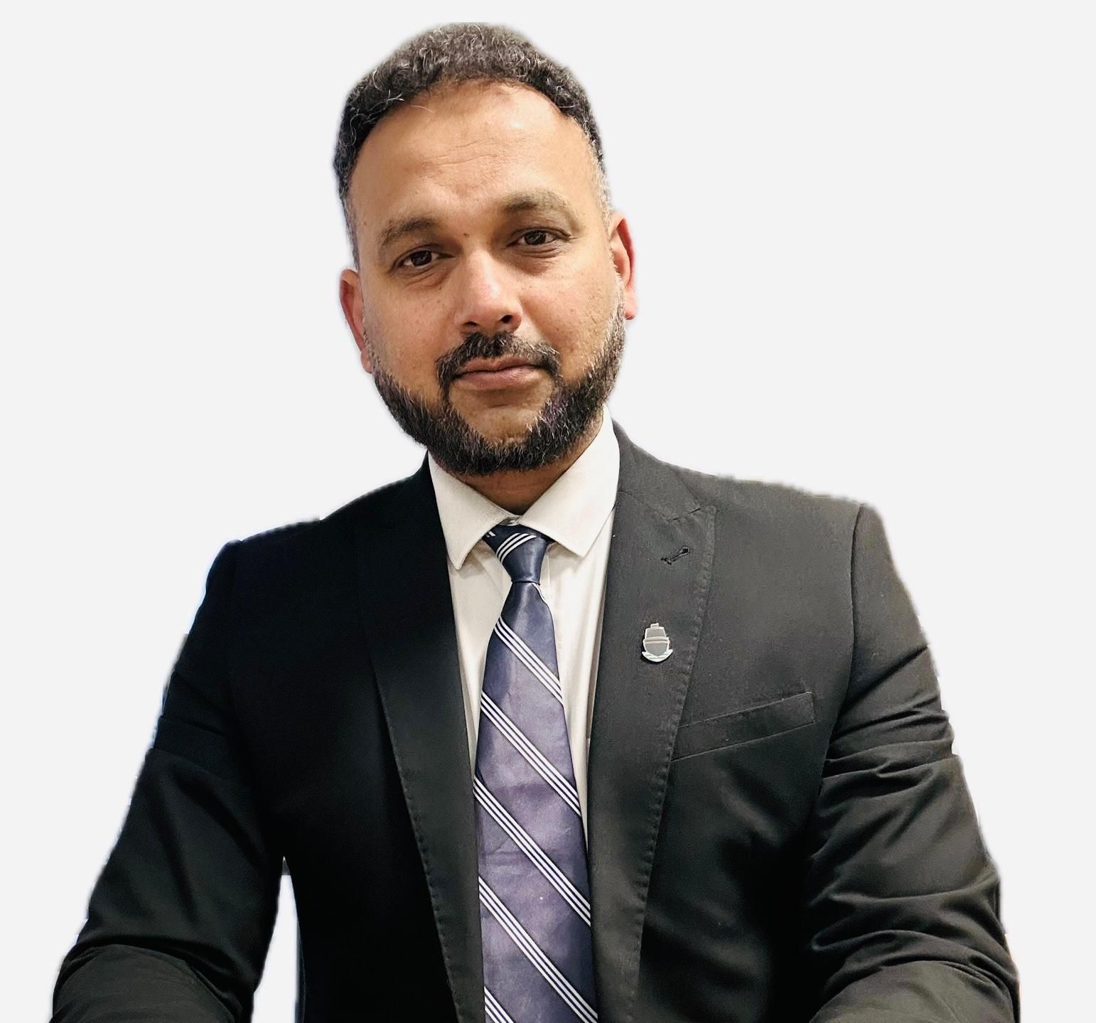 Man in suit, dark hair and beard, looking at camera with serious expression.