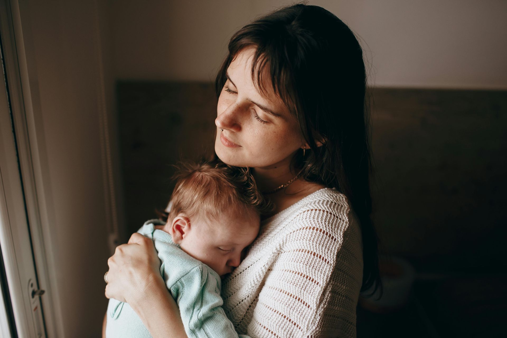 Woman cradles a sleeping baby in her arms, bathed in soft light.