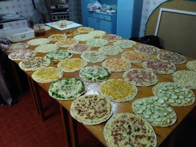 Várias pizzas dispostas sobre mesas na área de preparação da cozinha ou pizzaria.