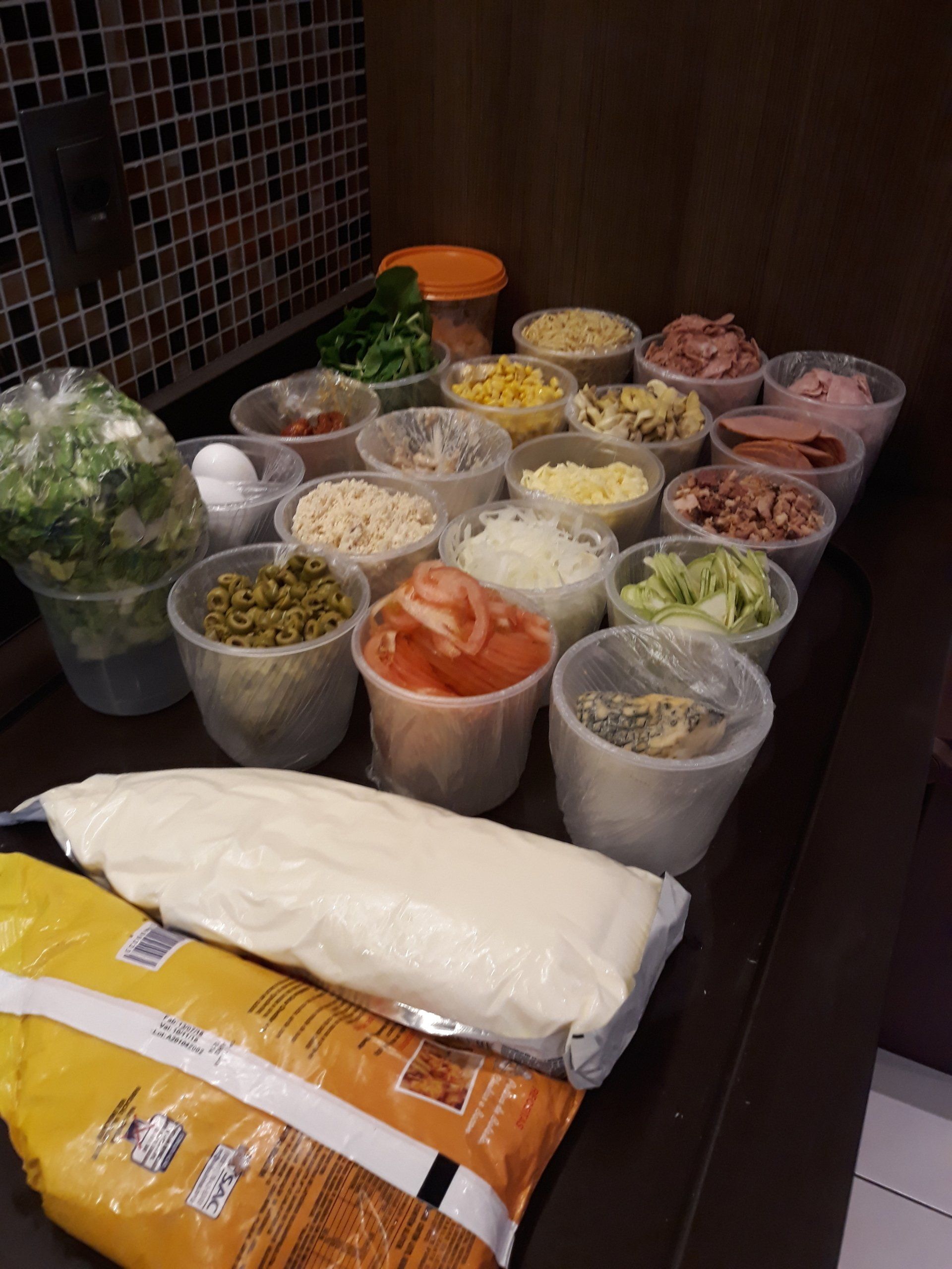 Tigelas variadas com ingredientes de salada já preparados e wraps embalados sobre a bancada da cozinha