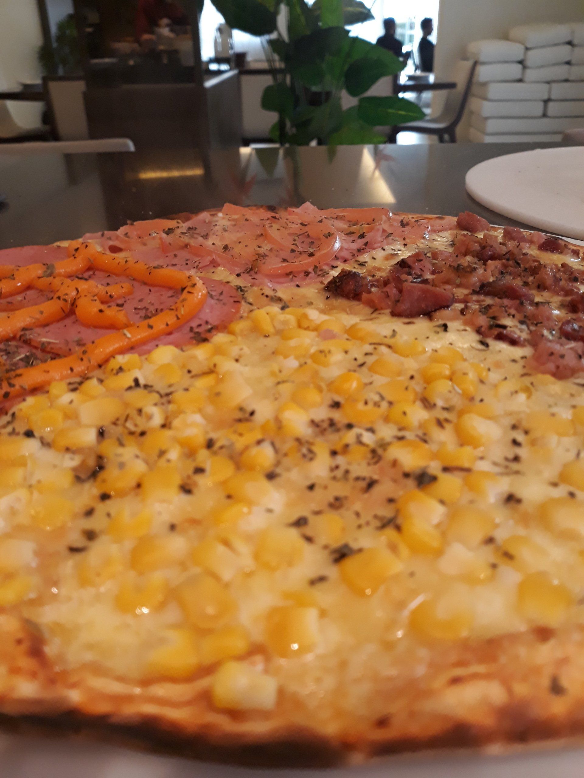 Fatia de pizza com milho, pepperoni e pimentão vermelho sobre uma mesa em um café.