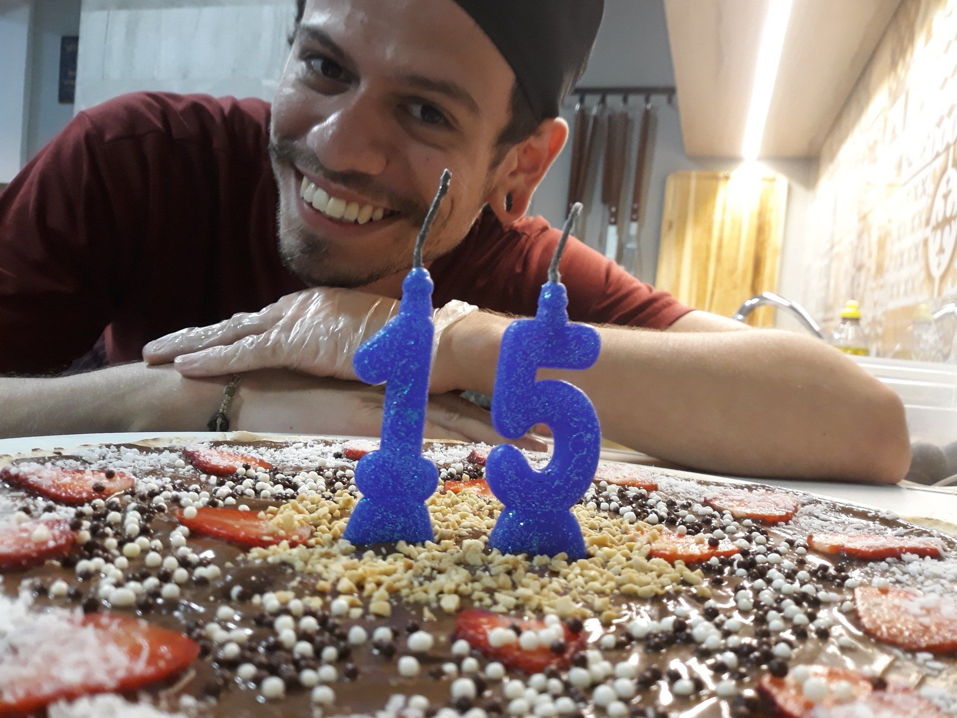 Pessoa sorridente debruçada sobre um bolo com velas azuis em formato de números 