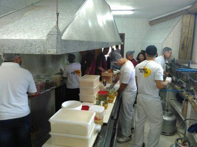 Cozinheiros de uniforme branco trabalhando em uma cozinha comercial movimentada com equipamentos de aço inoxidável.