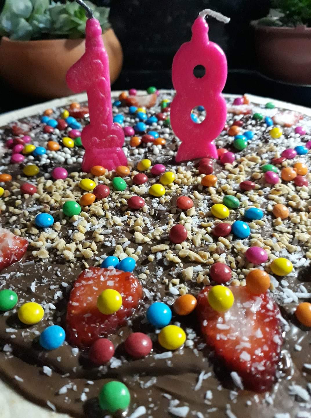 Bolo de chocolate coberto com granulado colorido e velas rosa em formato de números 