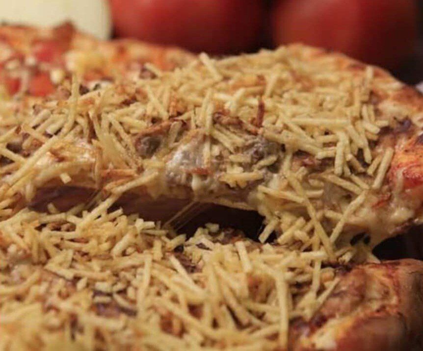 Pizza de pepperoni com queijo e coberta com palitos de batata crocantes em um prato.